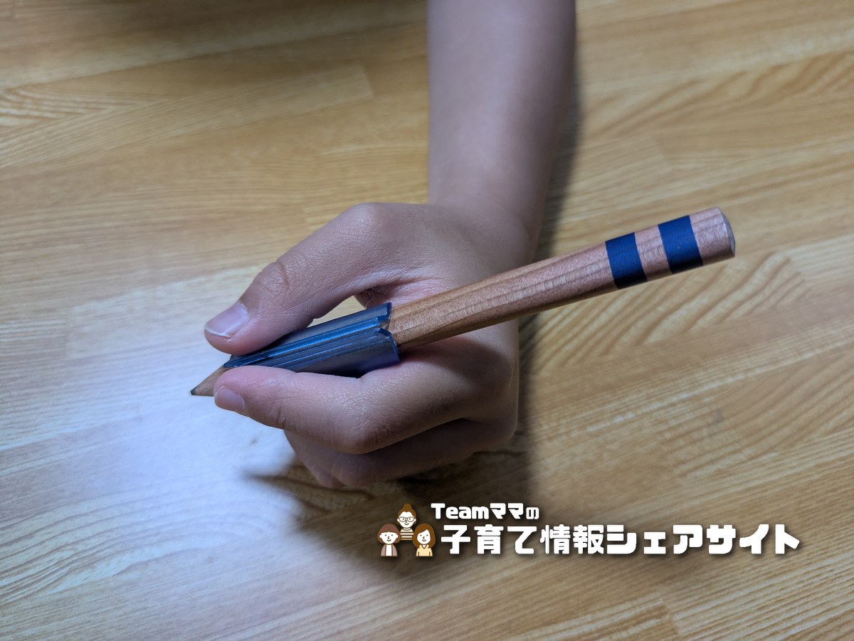 目玉クリップを付けた鉛筆を、親指と人差し指・中指の3本で持って書く練習をしている様子