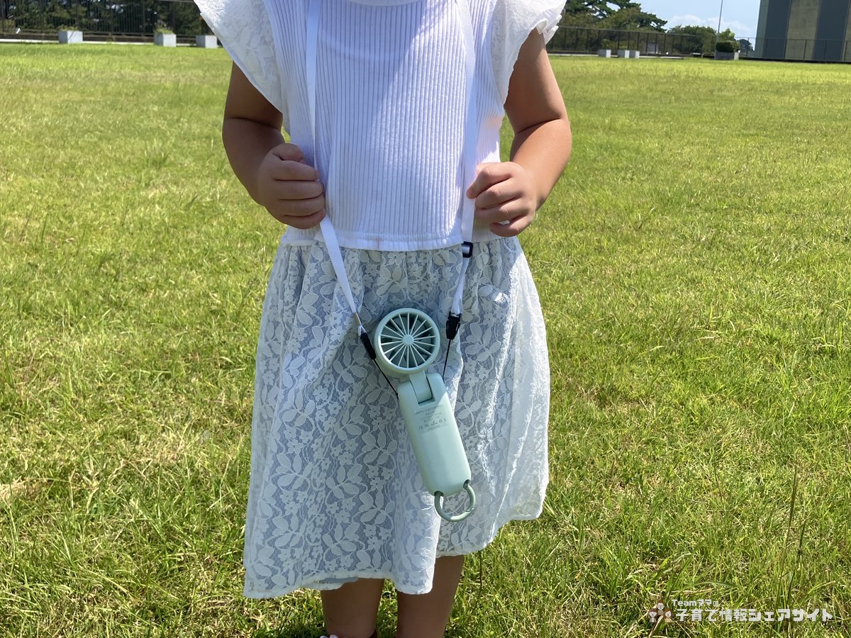 4歳の子どもが冷却プレートつきハンディファンを首から下げている様子 白い服とレースのスカート